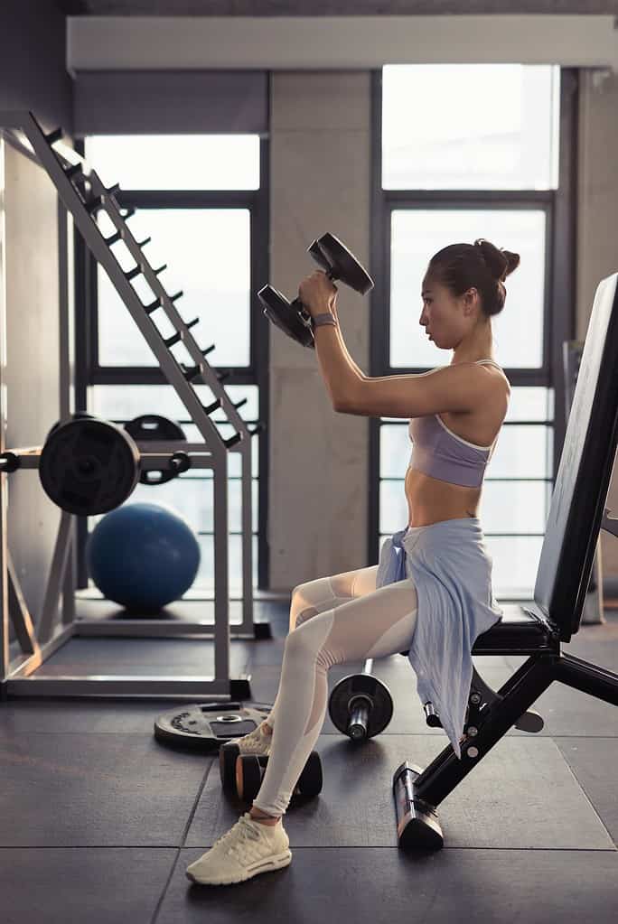 A woman performing a ballet conditioning exercise with light weights at the gym