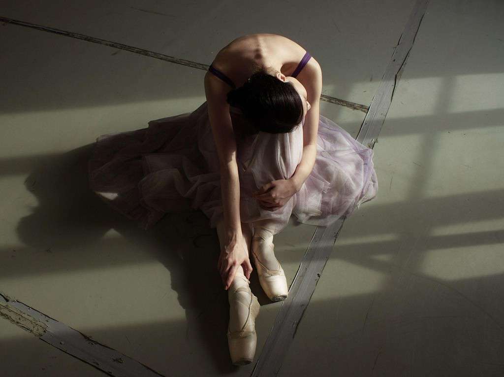 A ballerina sitting on the floor, struggling with mental health following ballet injuries