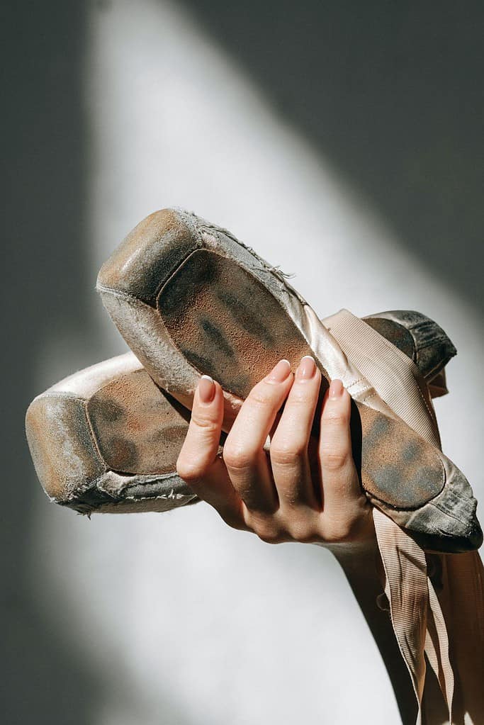 A woman holding up a pair of worn pointe shoes