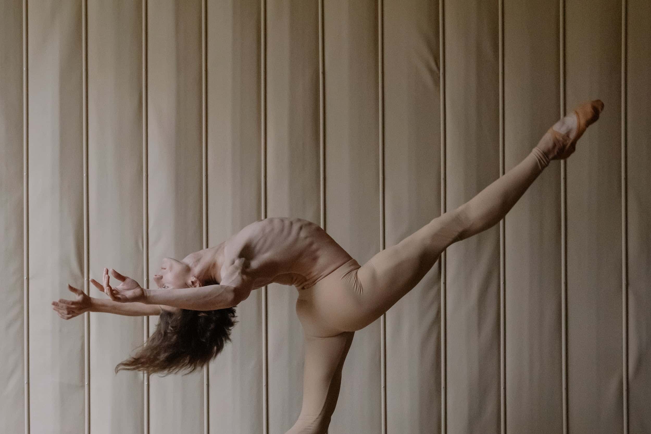 Contemporary male dancer in tan pants, extending leg upwards highlighting strong ballet technique