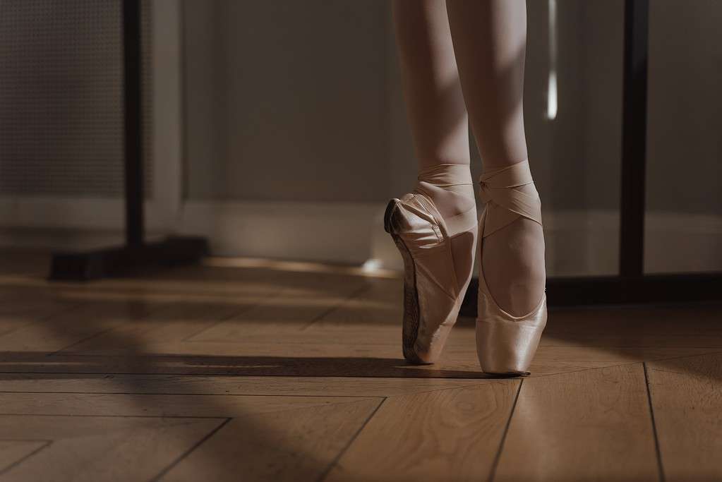 ballerina feet in pointe shoes on hardwood ballet flooring