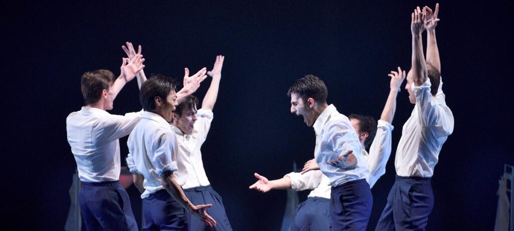 A group of male professional dancers on stage in white shirts and blue pants