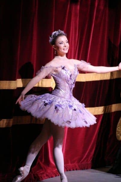 Female wearing a purple bell tutu against red curtain backdrop