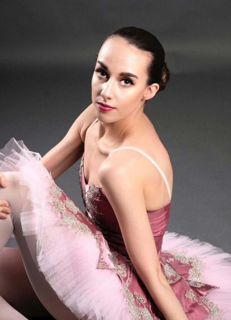 Ballerina sitting down wearing a pink ballet tutu with some embroidery