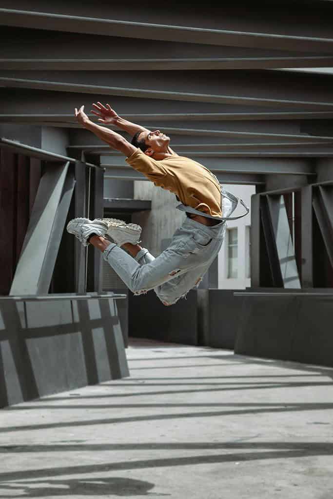 Male dancer jumping high in overalls outside