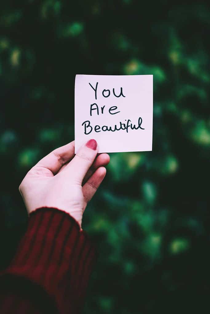 Lady holding up a short affirmation with the words 'you are beautiful'